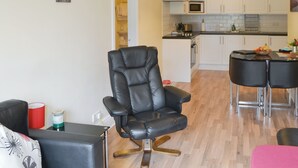 A modern living room with a black leather chair, a dining area with two bar stools, and a kitchen with white cabinets and a microwave. - Dove Cottage - UK3284 (Acklington, near Amble)