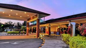 Entrada de hotel con zona de estacionamiento techada, sendero accesible y jardín cuidado.