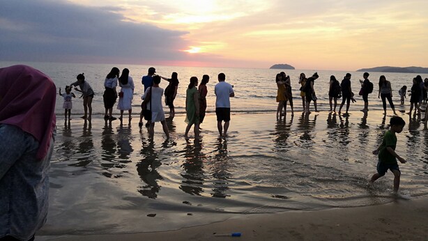 Un grupo de personas de pie en la playa al atardecer.