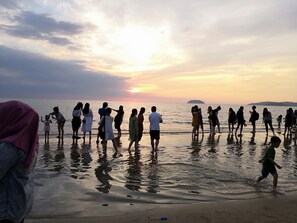 A group of people standing on a beach at sunset.
