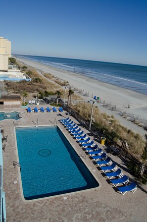 Relax by the pool with a view of the adjacent beach, surrounded by lounge chairs.