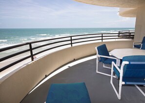 A balcony with a view of the ocean, a table, and blue chairs.