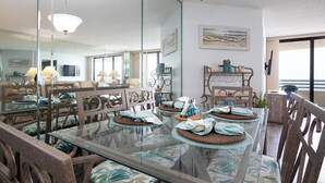 Un coin repas avec une table en verre, des chaises dotées de coussins à motifs et un grand miroir qui reflète la pièce.