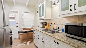 A compact kitchen with white cabinets, a stainless steel refrigerator, a microwave, and a sink with a knife block. - Beach Bungalow 3. Dog-Friendly. Steps from the beach! (San Diego)