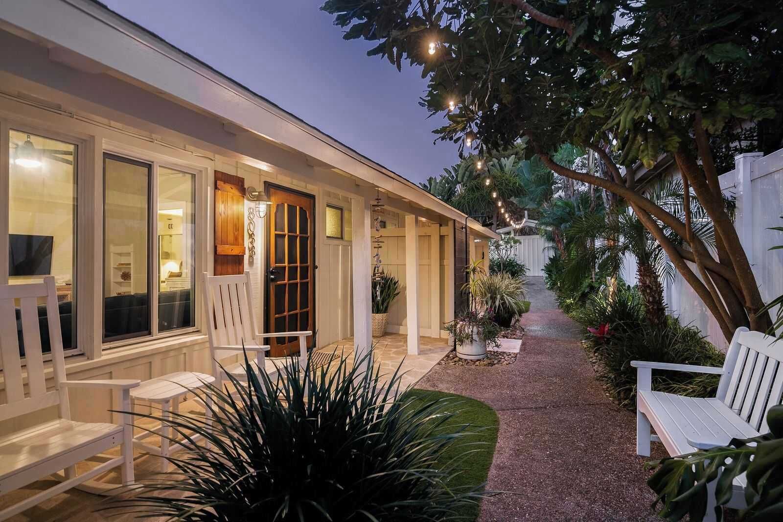 A covered outdoor area with a wooden door, white chairs, and potted plants.