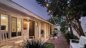 A covered outdoor area with a wooden door, white chairs, and potted plants. - Beach Bungalow 3. Dog-Friendly. Steps from the beach! (San Diego)