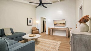A modern living room with a grey sofa, a round coffee table, a beige armchair, a TV on a wooden stand, and a ceiling fan. - Beach Bungalow 3. Dog-Friendly. Steps from the beach! (San Diego)