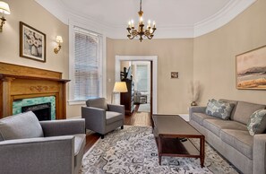 Un salon avec une cheminée, deux fauteuils, un canapé, une table basse et un lustre.