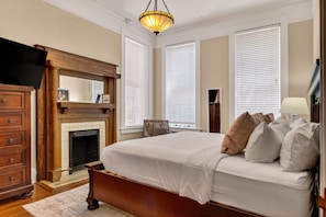 Une chambre à coucher avec un grand lit, une cheminée, une commode en bois et un téléviseur.