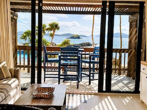 A room with a view of the ocean, a wooden deck, a sofa, and a table with a basket.