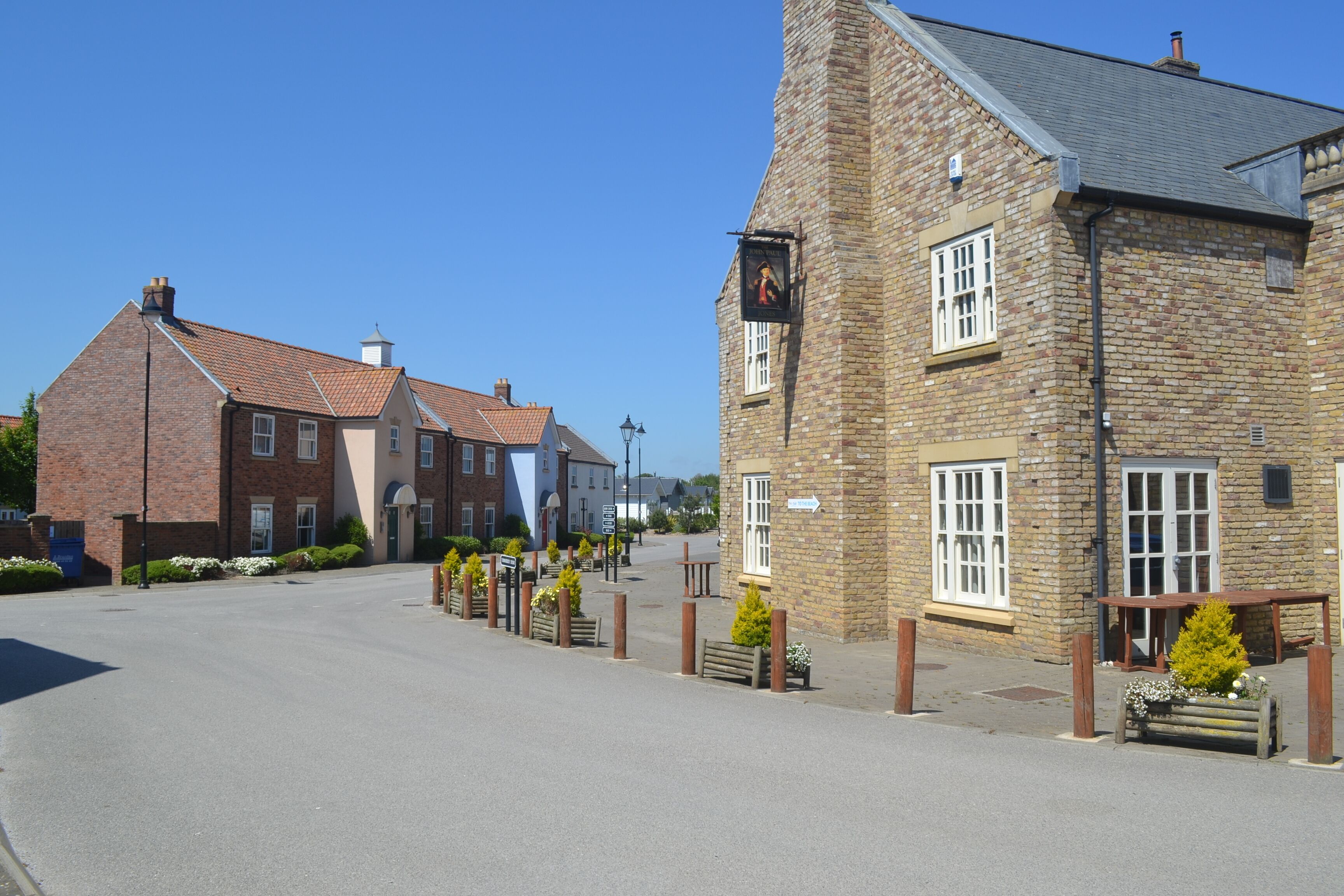 A quiet street with traditional brick buildings, a clear sky, and a bench with flowers.