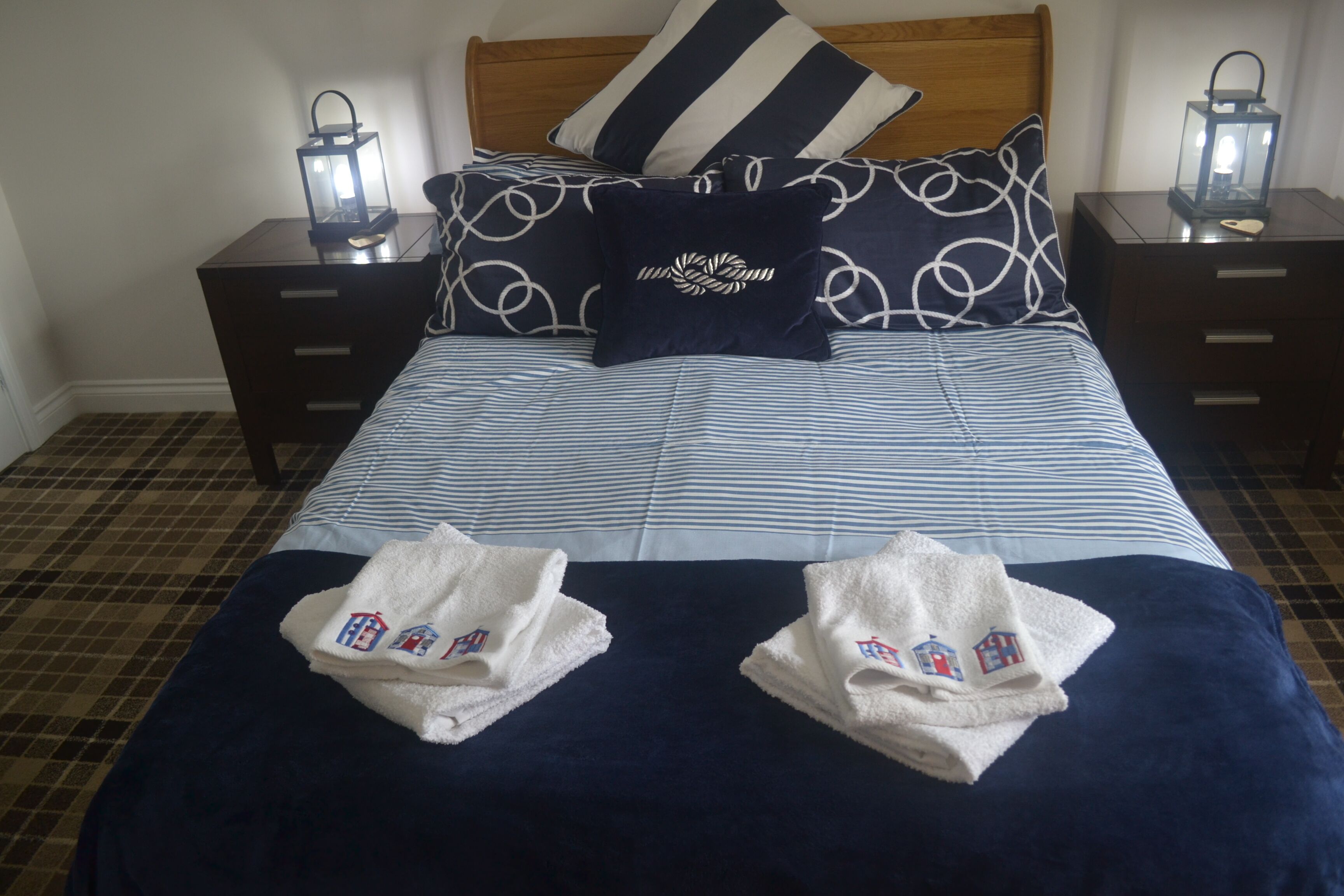 A neatly made bed with striped bedding, two pillows with a circular pattern, and two bedside tables with lanterns.
