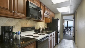 A kitchen with wooden cabinets, a black microwave, a stove, and a refrigerator. - Oceanfront Suite w/ Private Balcony + Official On-Site Rental Privileges (Myrtle Beach)