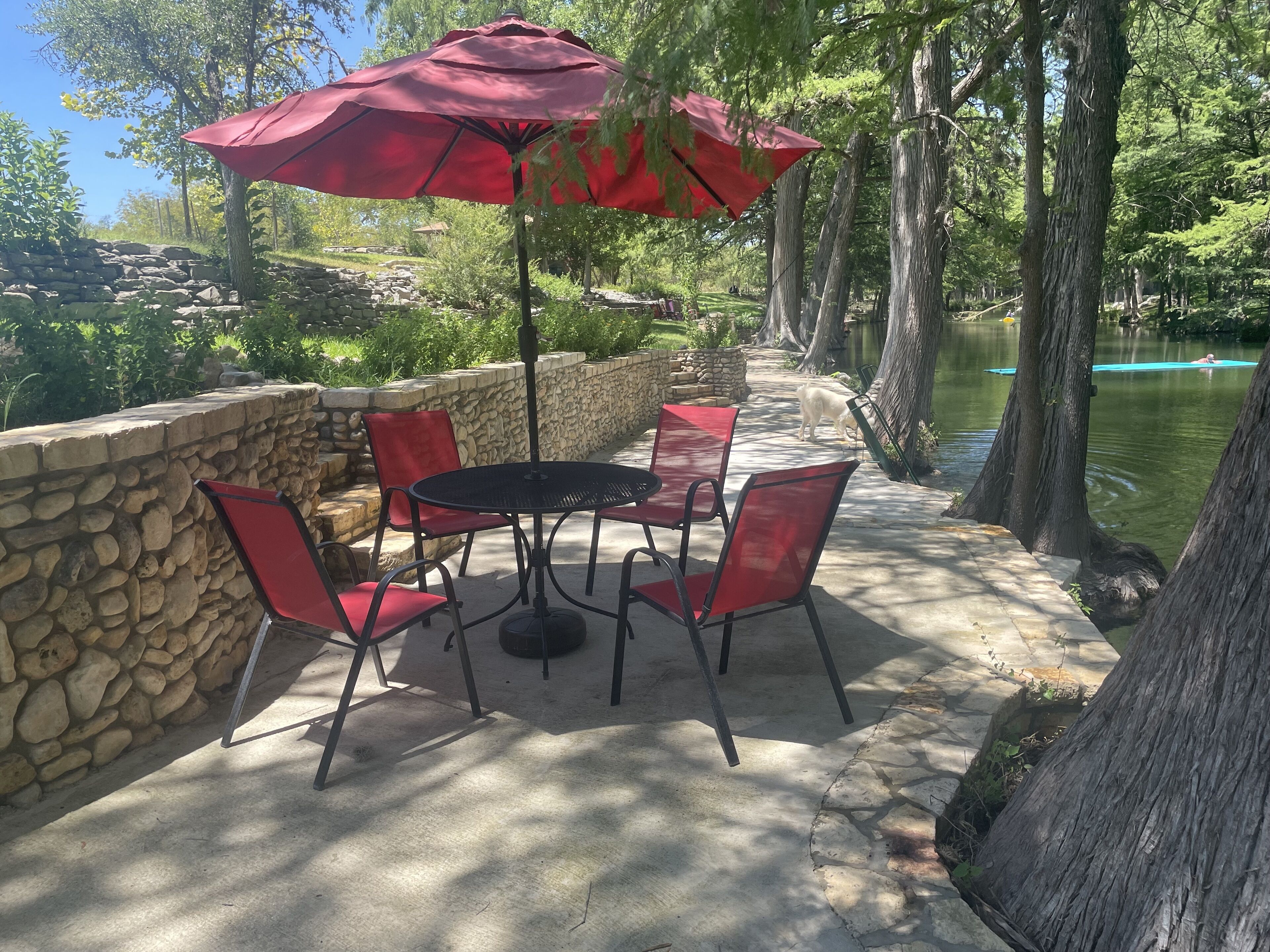 An outdoor patio with a stone wall, a round table with chairs, and a red umbrella.