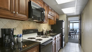 A kitchen with wooden cabinets, a black microwave, a stove, and a refrigerator.