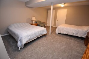 Quarto com duas camas, mesa de cabeceira, abajur e uma cadeira.