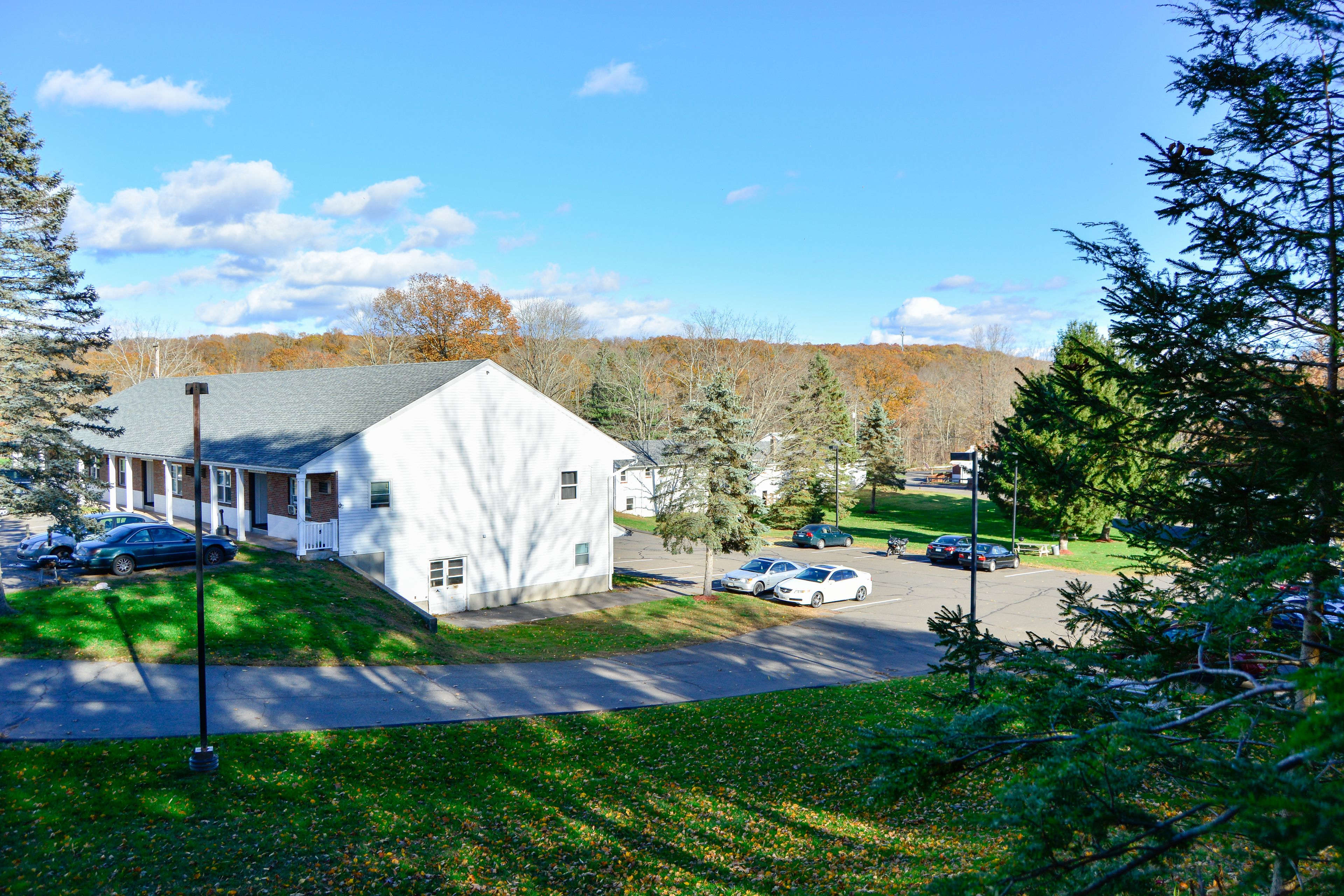 A white building with a sloped roof, surrounded by a parking lot and greenery.