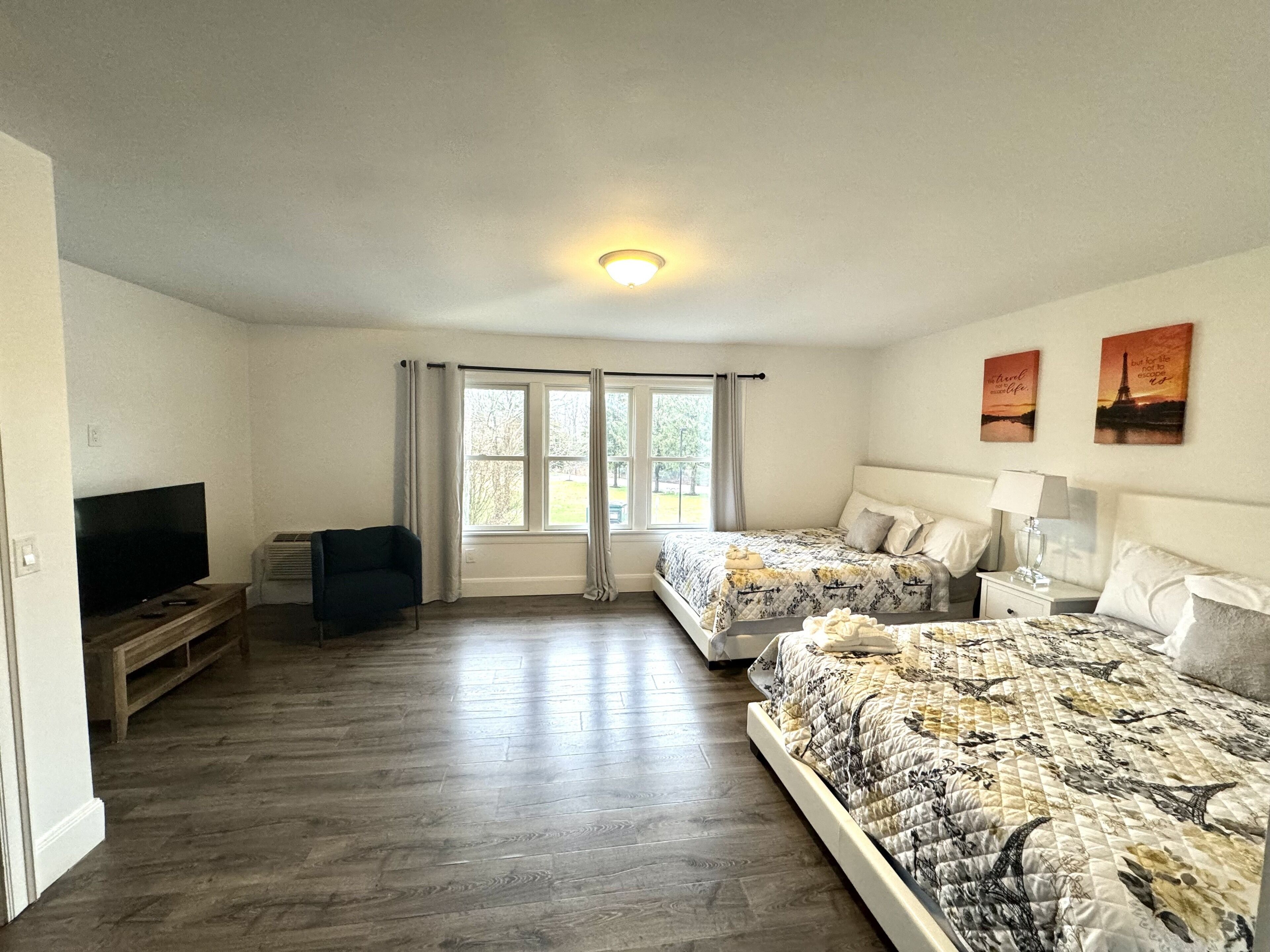 A bedroom with two beds, a TV, and a window with curtains.