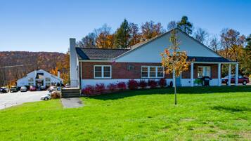A two-story building with a brick facade and a white roof, surrounded by a green lawn and trees with autumn foliage.
