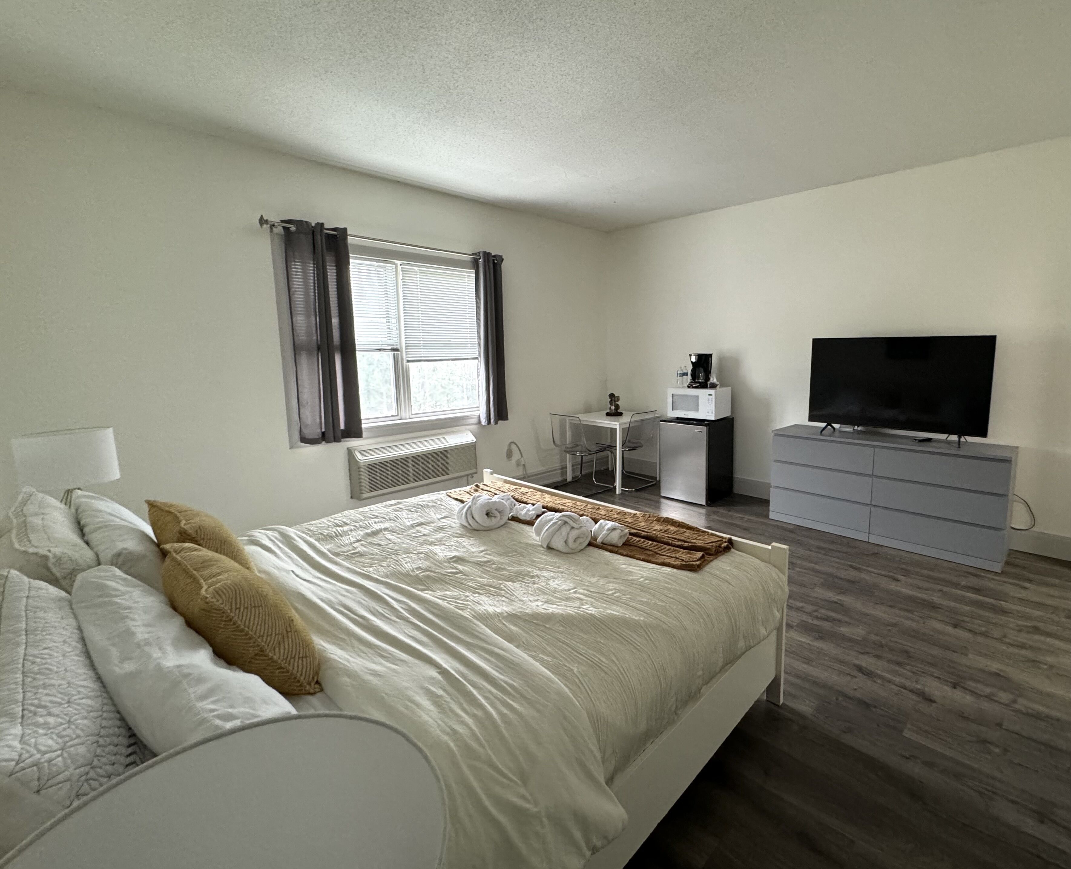 A bedroom with a bed, a TV, a dresser, a desk, and a window with curtains.
