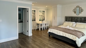 A bedroom with a large bed, a desk with chairs, and a dining area.