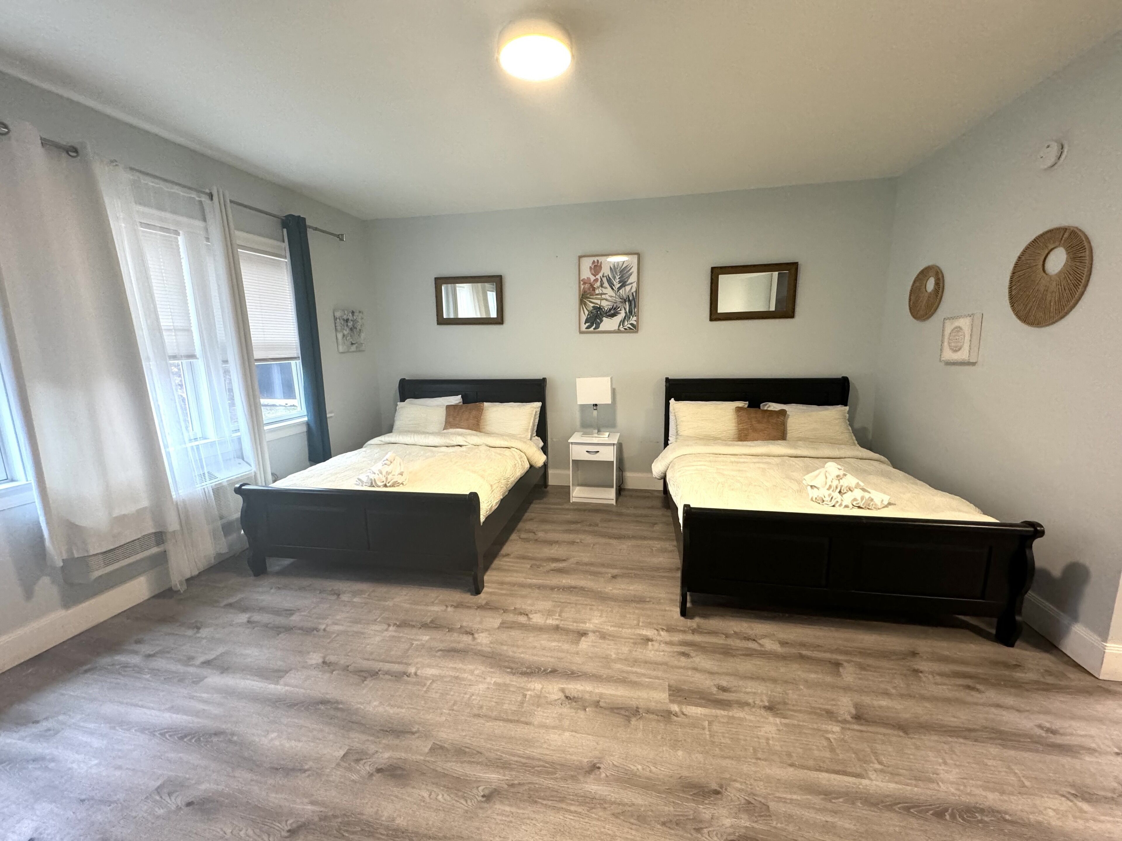 A bedroom with two beds, a nightstand, a mirror, and artwork on the wall.