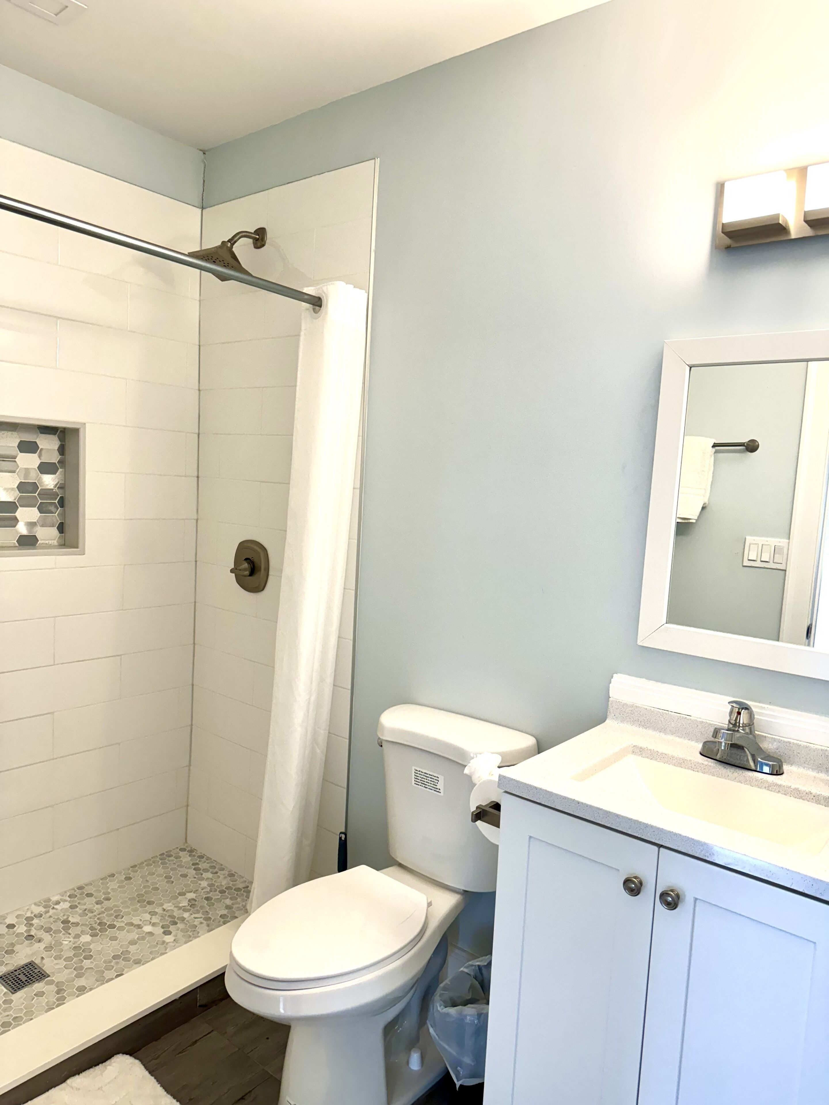 A bathroom with a shower, toilet, sink, and mirror.