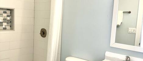 A bathroom with a shower, toilet, sink, and mirror.