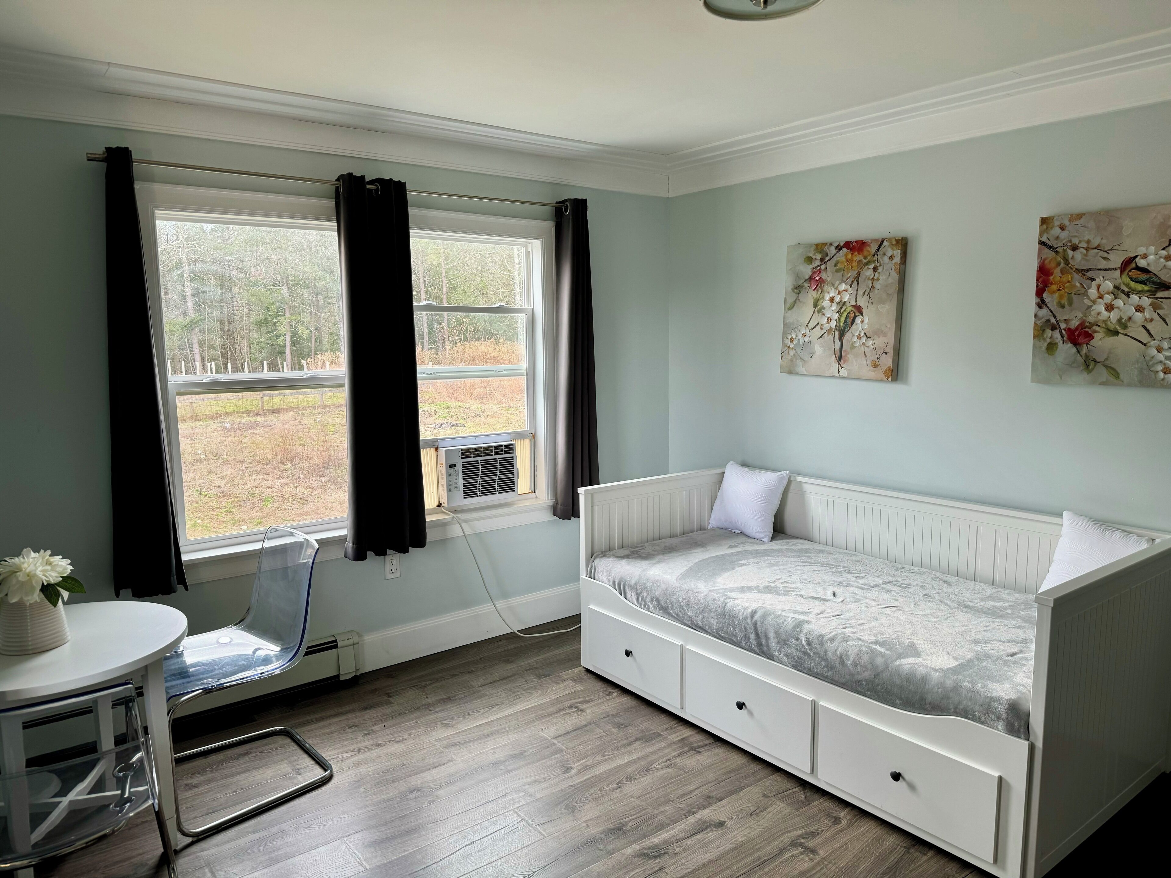 A bedroom with a bed, a window, a radiator, and a small table with a plant.