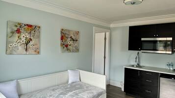 Quarto moderno com sofá branco, pintura de pássaros em um galho, cozinha com micro-ondas e pia.