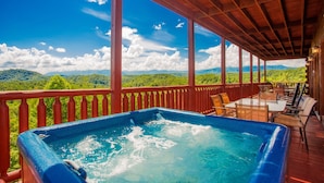 Ein Whirlpool auf einer Holzterrasse mit Blick auf grüne Hügel und einen klaren Himmel.