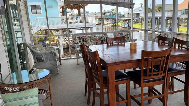 A covered outdoor dining area with a wooden table and chairs, surrounded by a glass enclosure. - Fisherman's Paradise-Closest Canal Rental to Bait,Gas,Restaurant& Bar by Boat (Galveston)