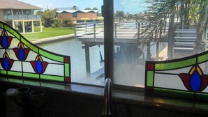 A view through a window with stained glass, a pool, and a building in the background. - Fisherman's Paradise-Closest Canal Rental to Bait,Gas,Restaurant& Bar by Boat (Galveston)