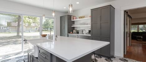 Una cocina moderna con una isla grande, armarios grises e iluminación colgante.