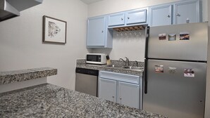 Eine kompakte Küche mit Granit Arbeitsplatten, einer Mikrowelle, einem Geschirrspüler und einem Kühlschrank mit Magneten.