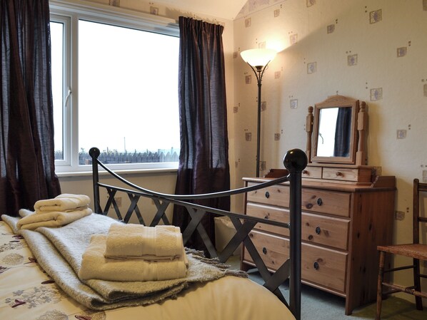 Une chambre à coucher avec un lit, une commode, un miroir et une fenêtre avec des rideaux.