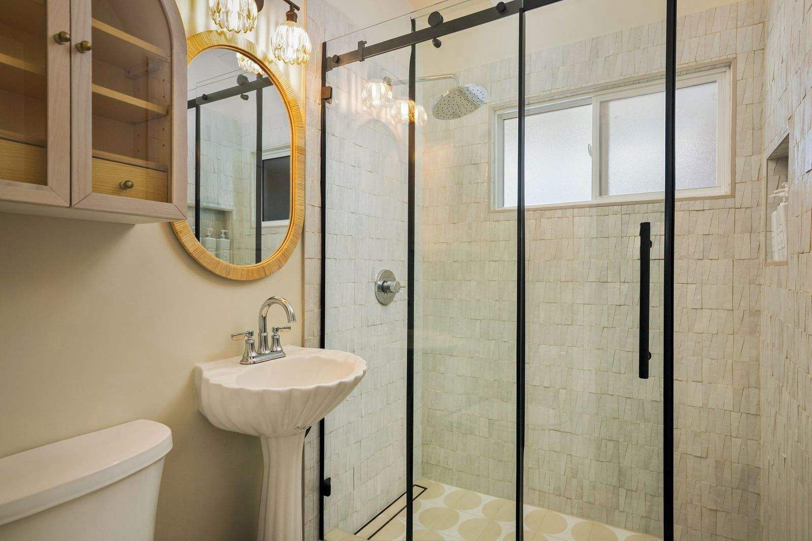 A bathroom with a glass shower enclosure, a white sink, and a wooden cabinet with a mirror.
