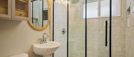 A bathroom with a glass shower enclosure, a white sink, and a wooden cabinet with a mirror.