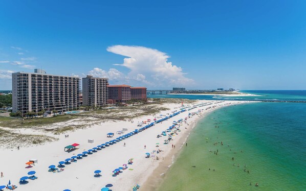 A beach resort with multiple high-rise buildings, a long stretch of beach with umbrellas, and clear turquoise waters.