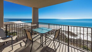Ein Balkon mit Glastisch und Stühlen, mit Blick auf einen Strand und den Ozean.