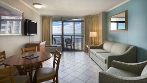 A hotel room with a dining table, chairs, a sofa, a TV, a lamp, and a balcony with a view of the city. - Beautiful Deluxe Angle Oceanfront Suite + Official On-Site Rental Privileges (Myrtle Beach)