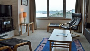 Une chambre d’hôtel équipée d’une télévision, d’un bureau, d’une chaise et offrant une vue sur le paysage urbain grâce à de grandes fenêtres.