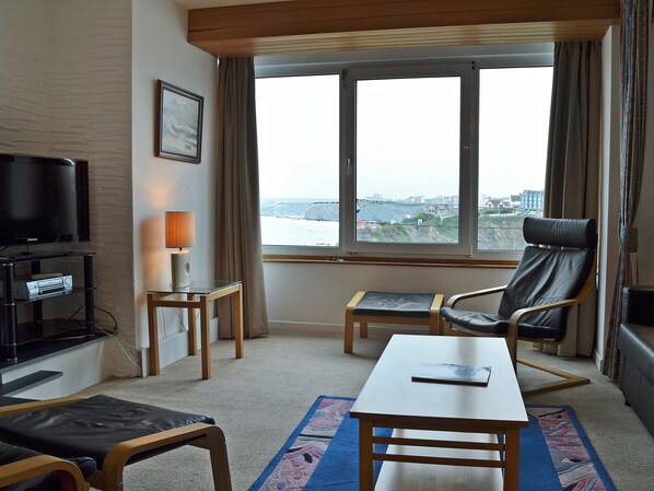 Ein Hotelzimmer mit Fernseher, Schreibtisch, Stuhl und Blick auf eine Stadtlandschaft durch große Fenster.