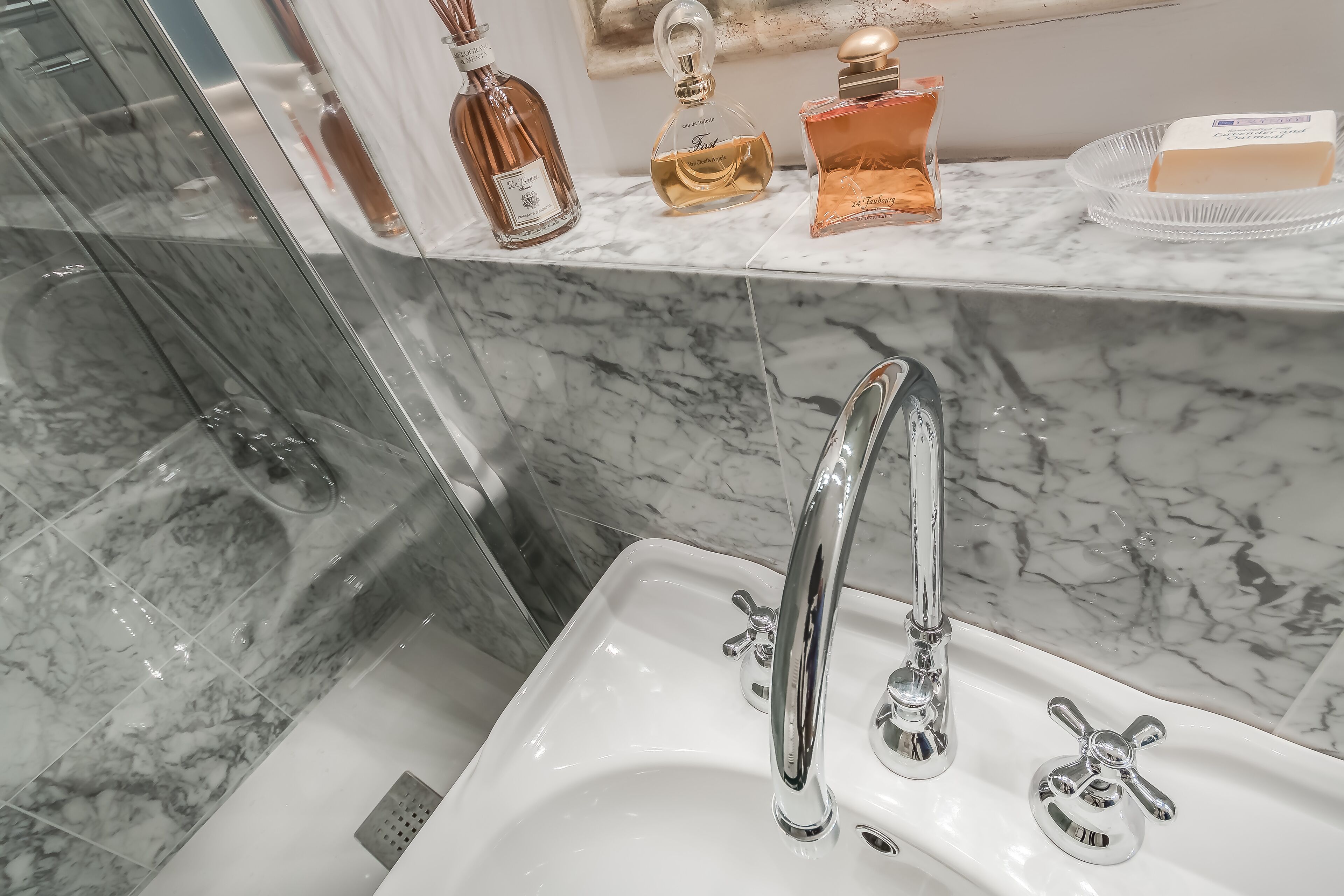 Un bany amb un lavabo de marbre, aixetes cromades i una cabina de dutxa de vidre.