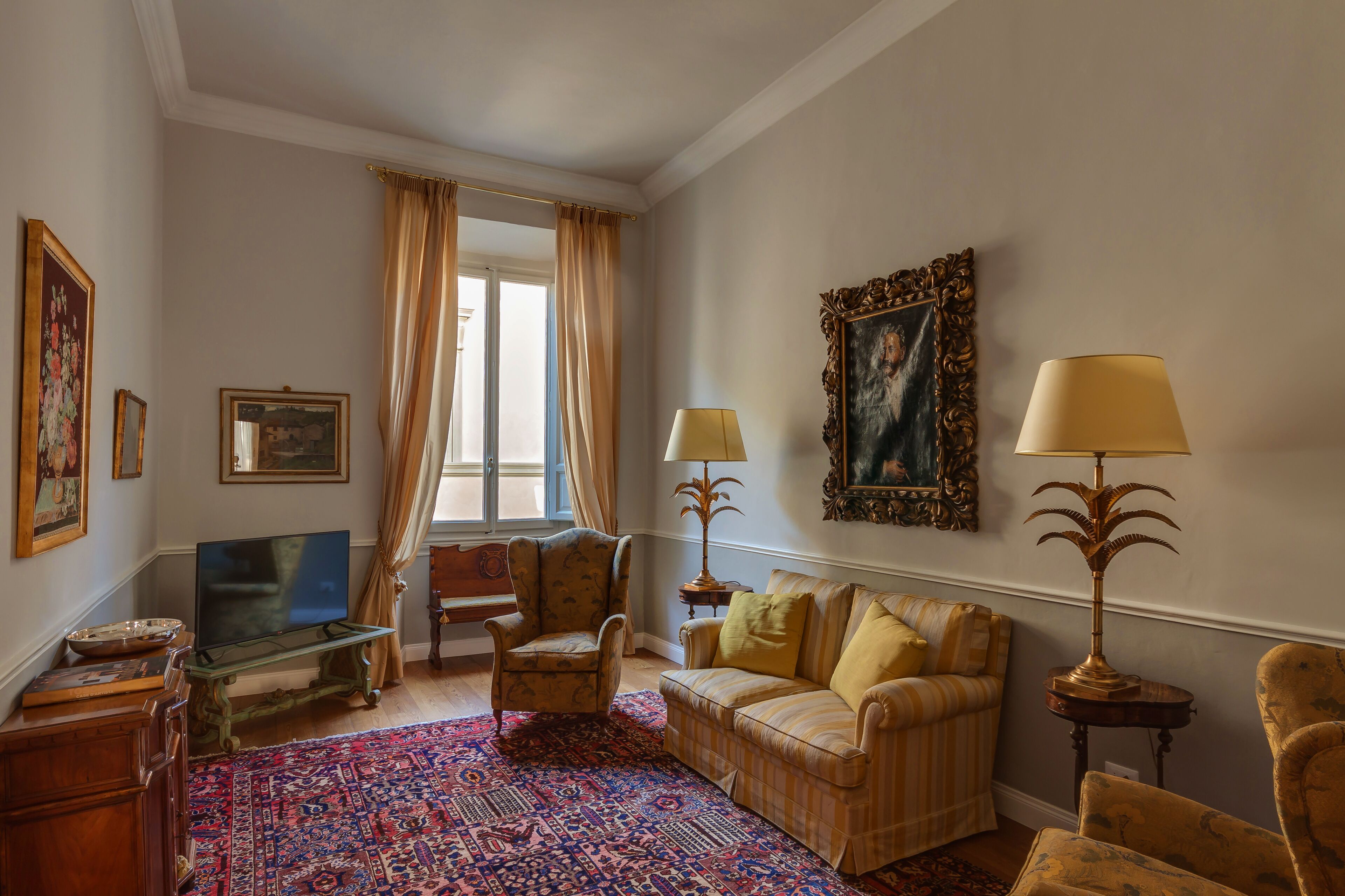 A living room with a television, armchairs, a sofa, patterned rug, and decorative lamps.