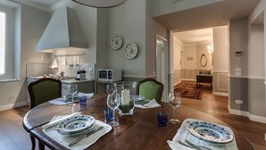 A dining area with a wooden table set for four, surrounded by chairs. There is a chandelier above the table, and a microwave and oven are visible in the background. - Beautiful apartment at one step from the Dome. Perfect for families! (Florence)
