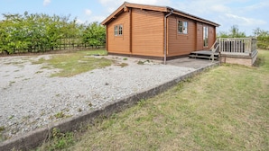 A small wooden cabin with a gravel driveway and a wooden deck.