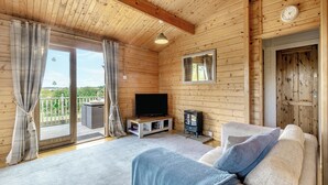 A cozy cabin interior with a wooden ceiling, a sofa, a television, and a sliding glass door leading to an outdoor area.