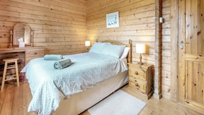 A wooden cabin bedroom with a bed, bedside tables, a mirror, and a door.