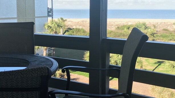 Uma varanda com vista para o oceano, uma mesa pequena e uma cadeira.